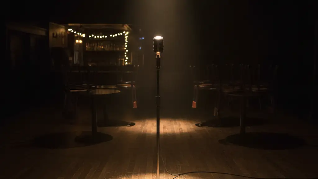 Empty stage with a single microphone stand under a spotlight in a music venue.