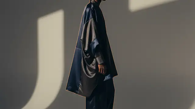 A silhouetted figure wearing high-concept loungewear against a minimalist, shadowed studio background.