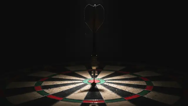 A single dart perfectly embedded in the bullseye of a dartboard, dramatically lit.