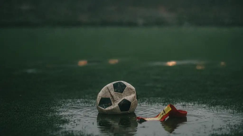 Deflated soccer ball and captain's armband on a wet, dark soccer pitch at dusk.