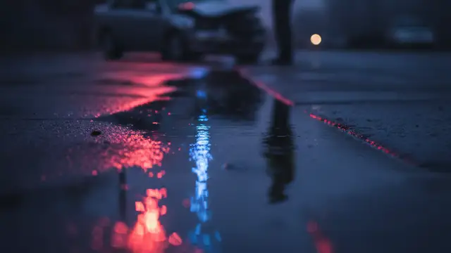 Emergency lights reflecting in a wet street, hinting at a car accident.