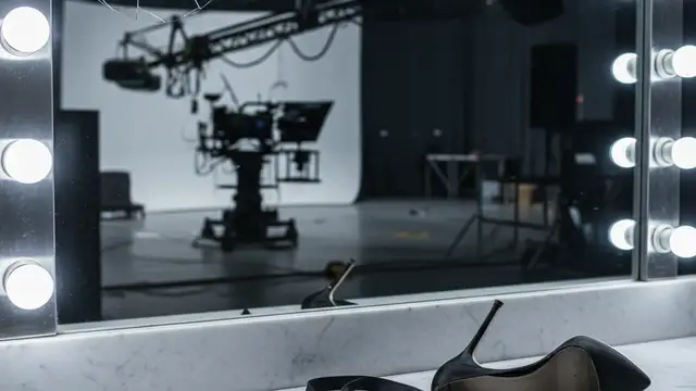 A cracked vanity mirror bulb and a discarded high-heeled shoe in an empty studio.