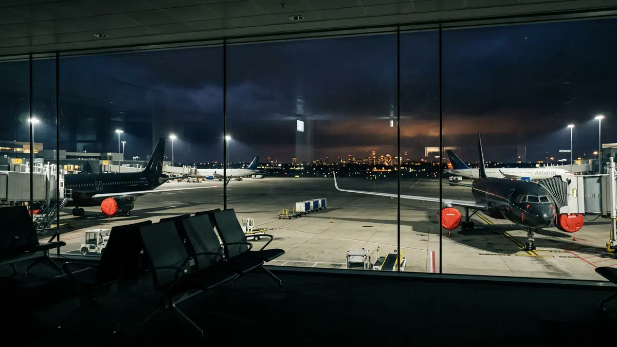 Grounded airplanes on a dark airport tarmac at night behind a glass terminal window.