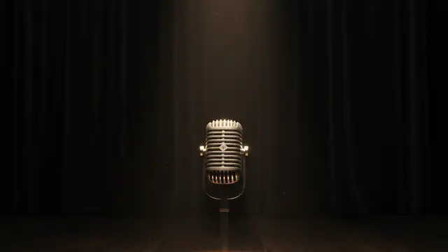 A vintage microphone rests on an empty stage under a single spotlight.