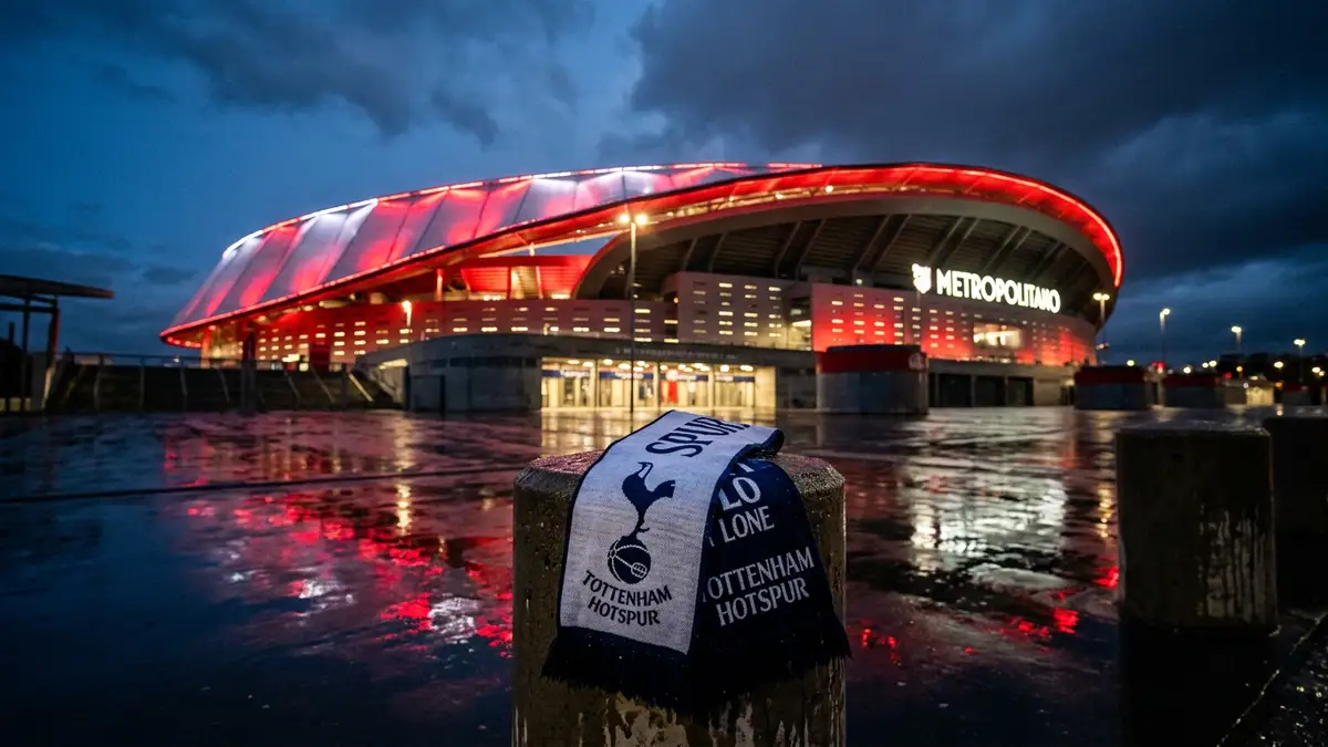 A Tottenham scarf draped on a bollard outside the glowing Metropolitano Stadium at night.
