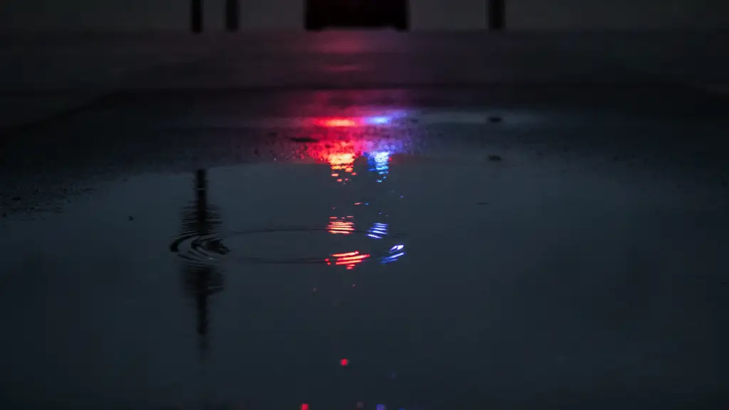 Emergency lights reflecting in a puddle near a taped-off beach entrance at dusk.