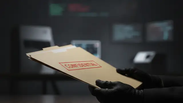 Gloved hand holding a confidential file folder on a dark desk.