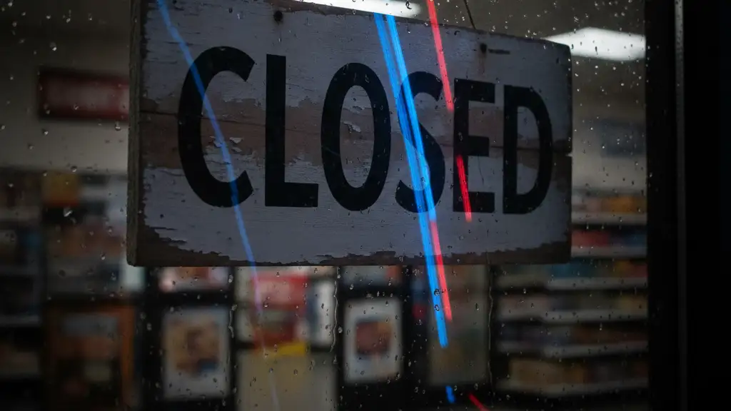 Close-up of a 'CLOSED' sign reflecting emergency lights on a rainy window.