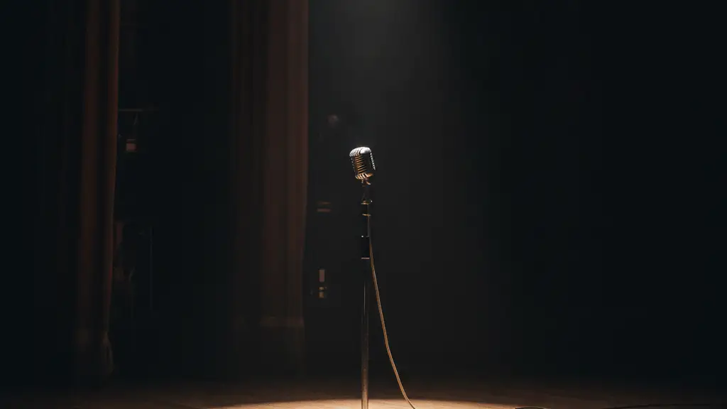 A lone, vintage microphone stand under a single spotlight on an empty stage.