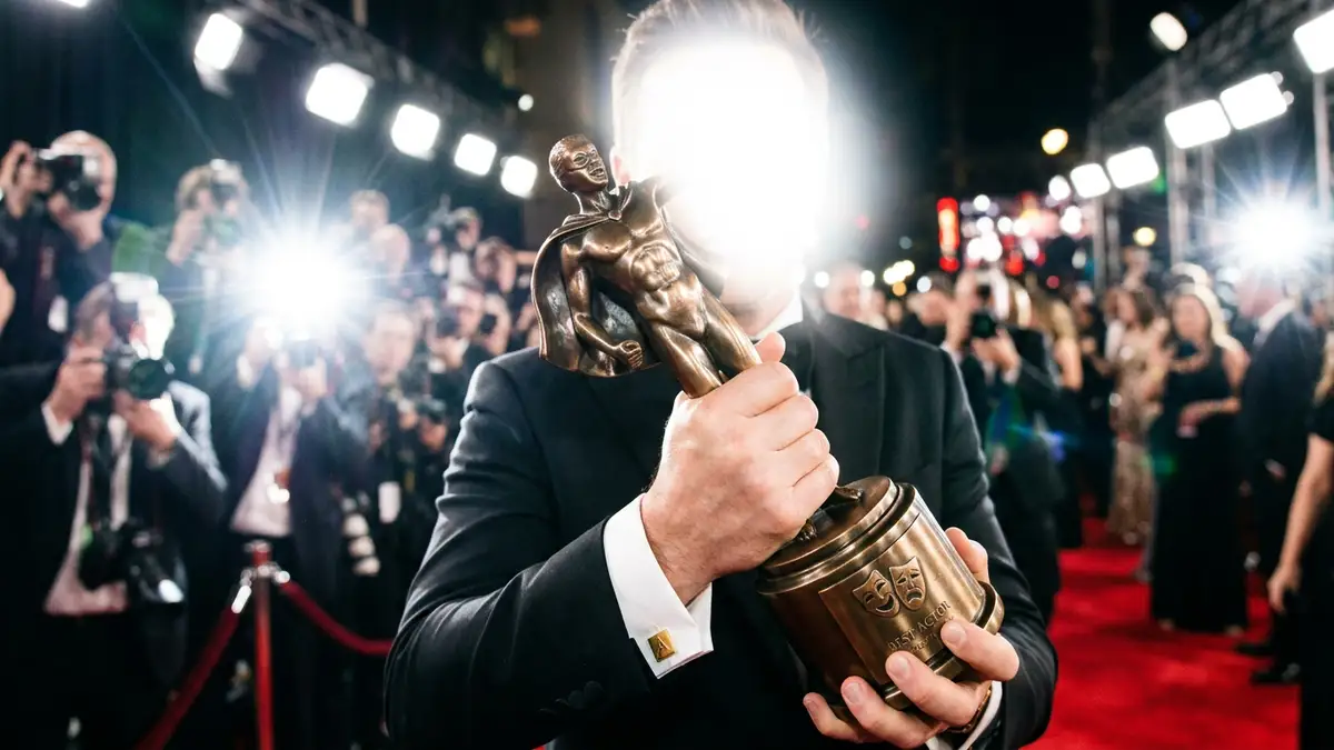 A close-up of a bronze award trophy held against a backdrop of bright camera flashes.