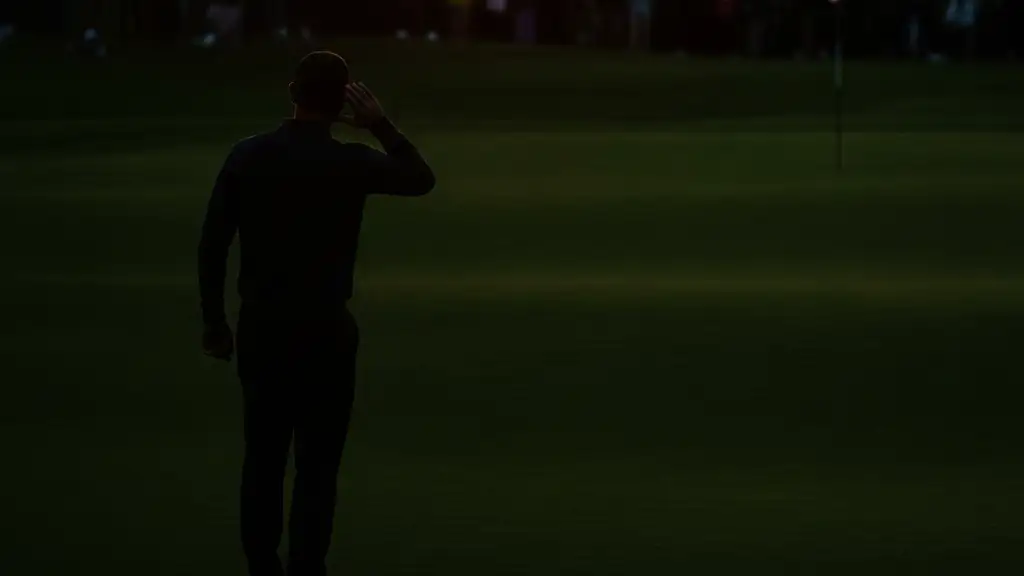 Silhouette of a golfer cupping their ear to a blurred crowd on a golf course.