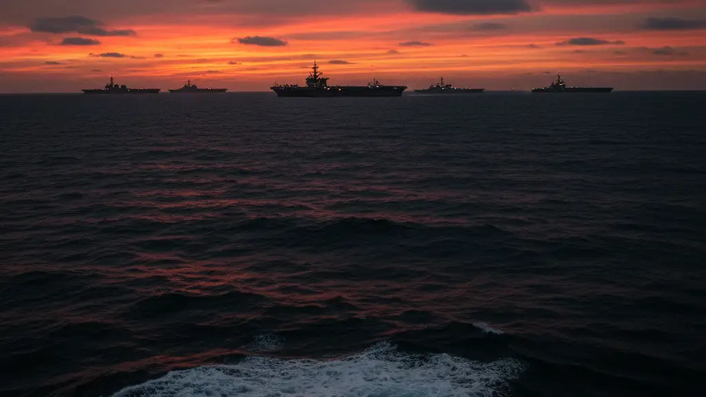 Silhouettes of a naval carrier strike group on the horizon during a dark sunset.