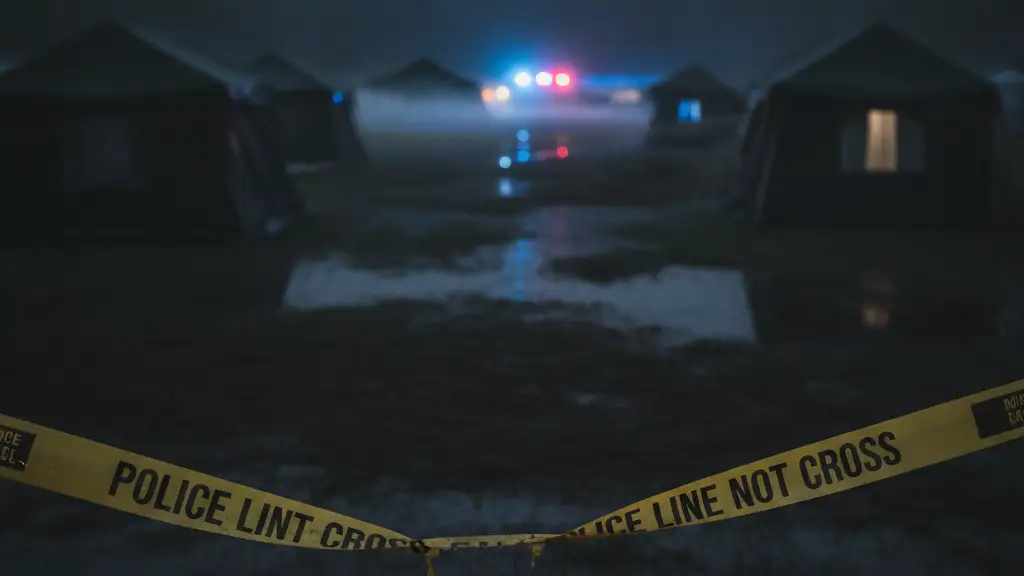 Police tape at a campsite with blurred emergency lights in the background.