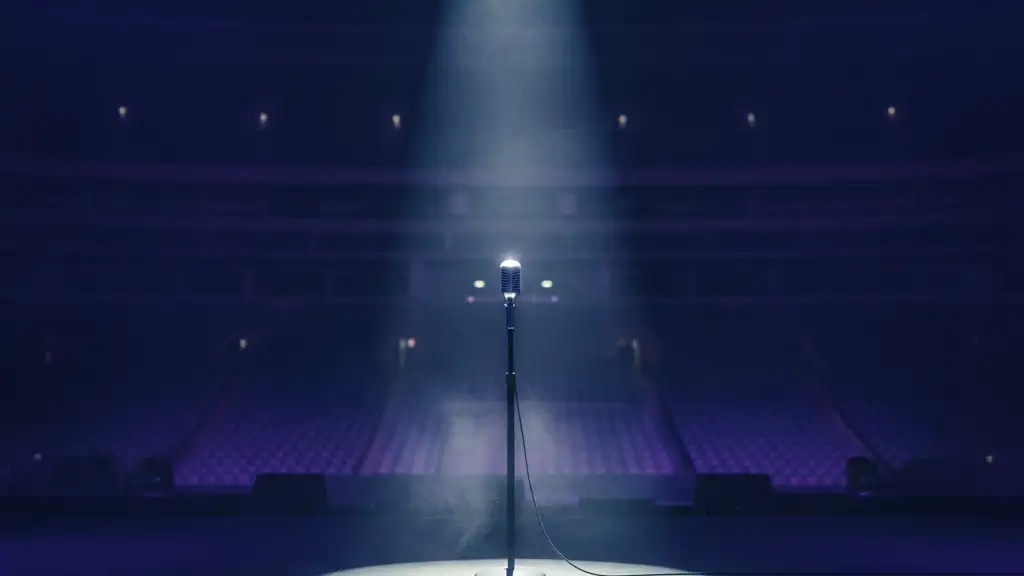 A lone microphone stand under a single spotlight on an empty stadium stage.