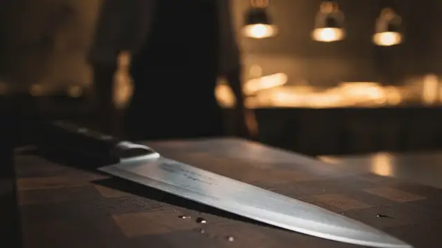 Chef's knife on cutting board, blurred figure in background.