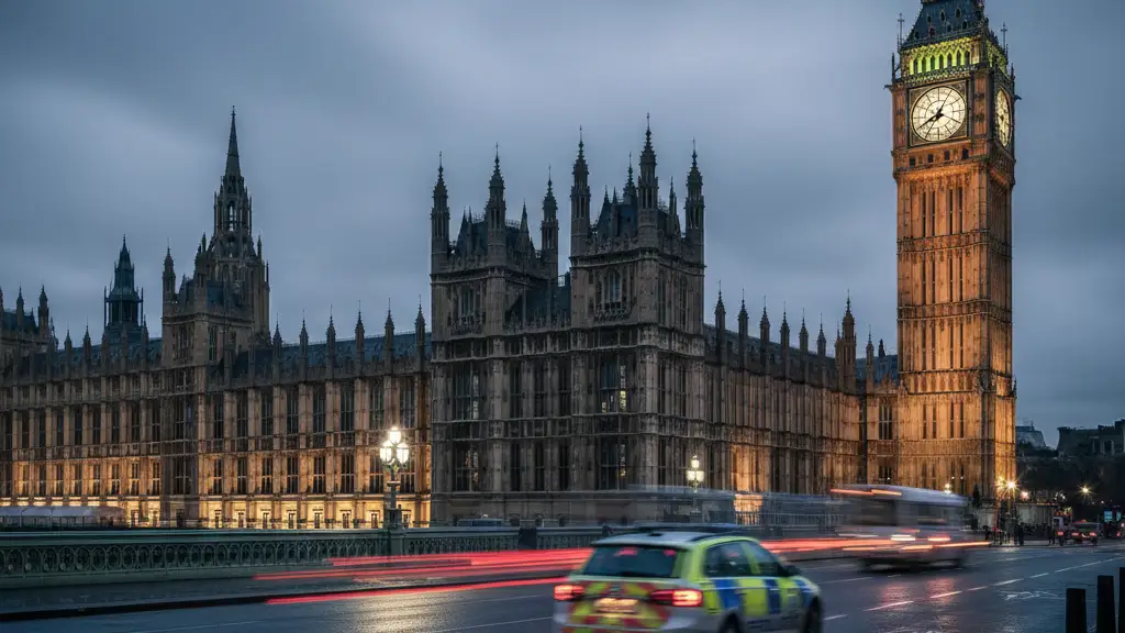 The Palace of Westminster at dusk with blurred emergency vehicle lights reflecting on wet pavement.