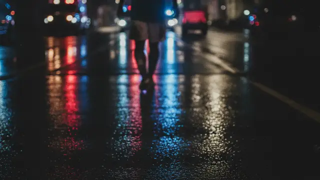Silhouette of a soccer player's lower leg and boot, with police lights reflecting on wet ground.