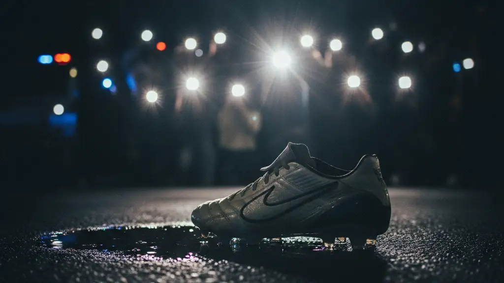 Close-up of a football boot with paparazzi flashes in the blurred background.
