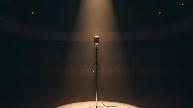 A spotlight shines on an empty microphone stand on a stage.