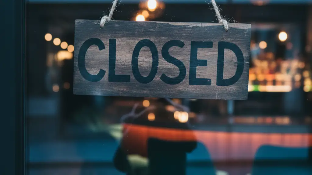 A 'Closed' sign hangs on a glass door overlooking a blurred, empty upscale bar interior.