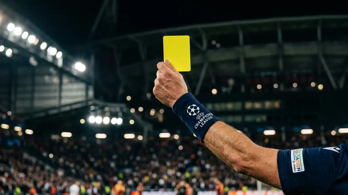 A referee's hand holding a yellow card against blurred stadium lights at night.