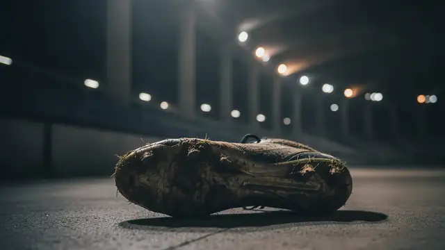 A muddy football boot on a concrete floor in a dimly lit stadium tunnel.
