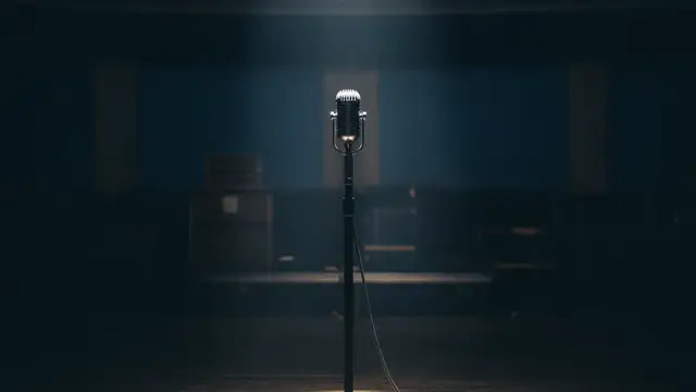 A lone vintage microphone stand under a single spotlight on an empty, dark stage.