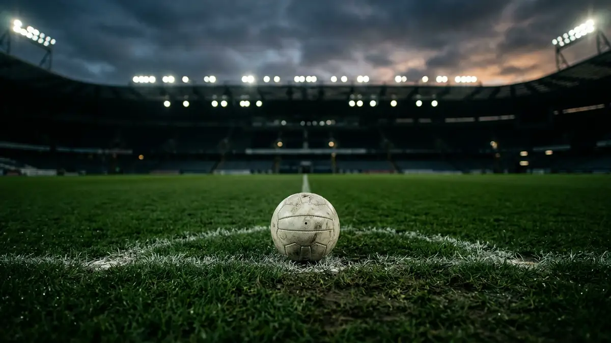 A lone football sits on a stadium pitch under bright lights at twilight.