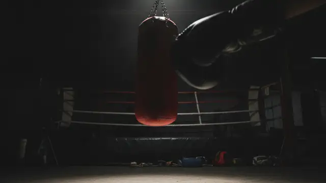 A blurred, gloved fist in motion, narrowly missing a speed bag in a dimly lit boxing gym.