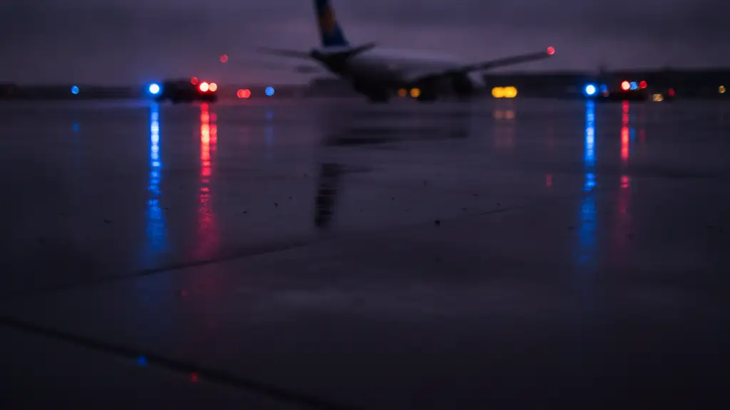 Emergency lights reflecting on wet tarmac with a distant airplane tail.
