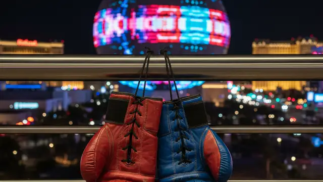 Boxing gloves hanging in front of the glowing Las Vegas Sphere at night.