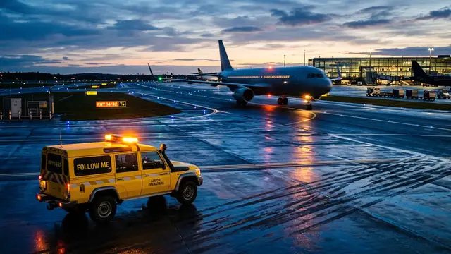 An airport tarmac at dusk with a blurred passenger plane taxiing in the background.