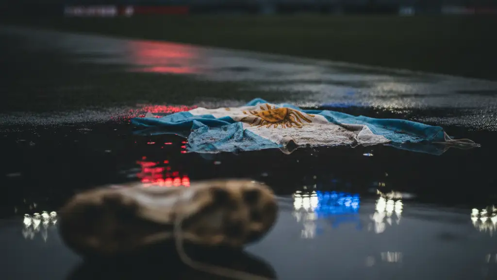 Tattered flag on wet stadium ground, reflecting distant lights, with a muddy football boot.