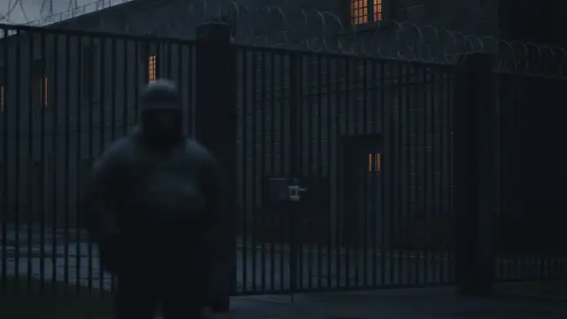 Exterior of a high-security psychiatric hospital at dusk with a barred window.