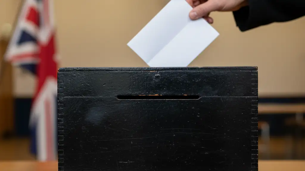 A hand placing a folded ballot paper into a black wooden ballot box.