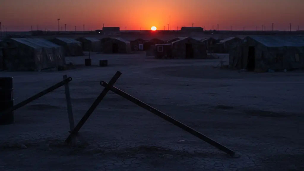 Silhouette of a military camp with police tape in the foreground at dusk.