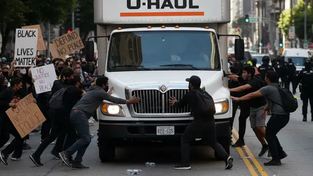 A white U-Haul truck driving through a crowd of protesters on a Los Angeles street.
