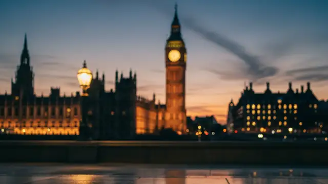 A discarded blue political rosette on a damp London pavement with Parliament blurred in background.
