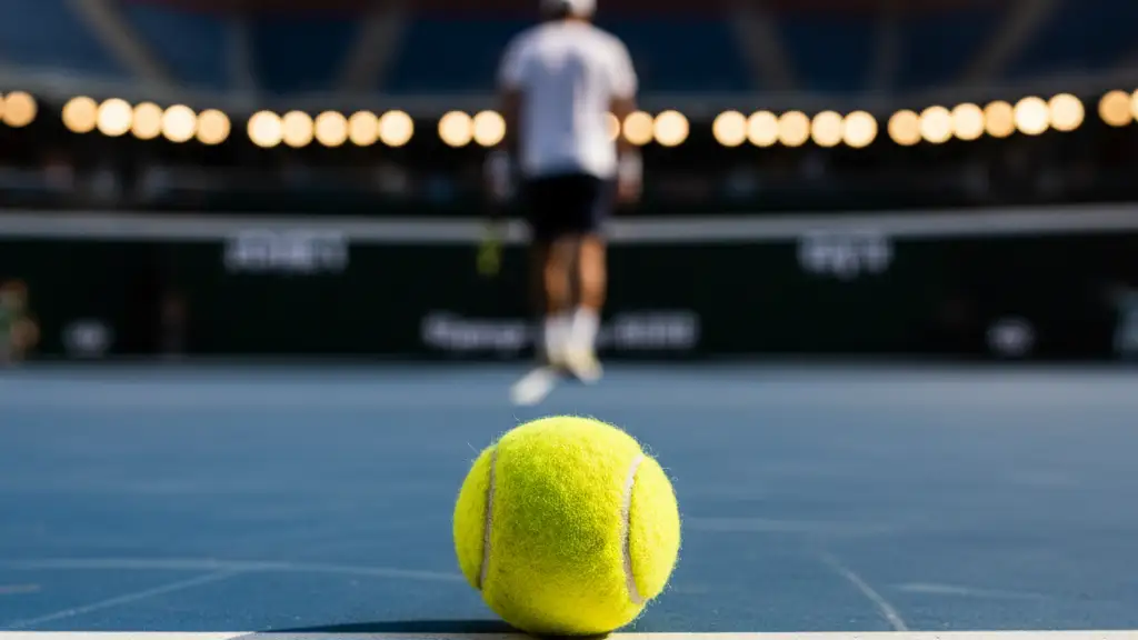 A single tennis ball rests on a blue court as a blurred figure walks away.